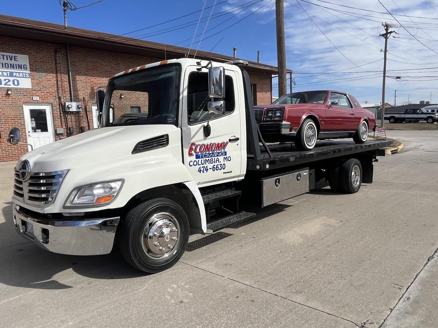 Economy Towing flatbed carrying a red classic car